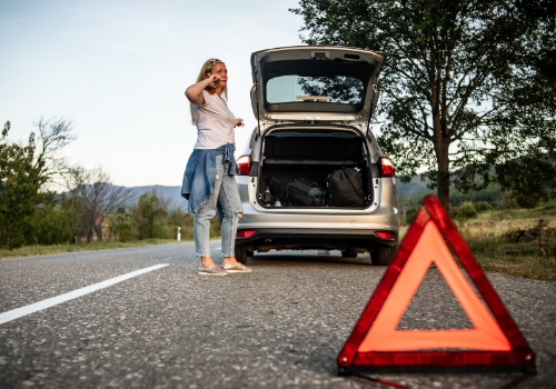 Woman out of broken-down car on the phone and with the signalling triangle already on the road